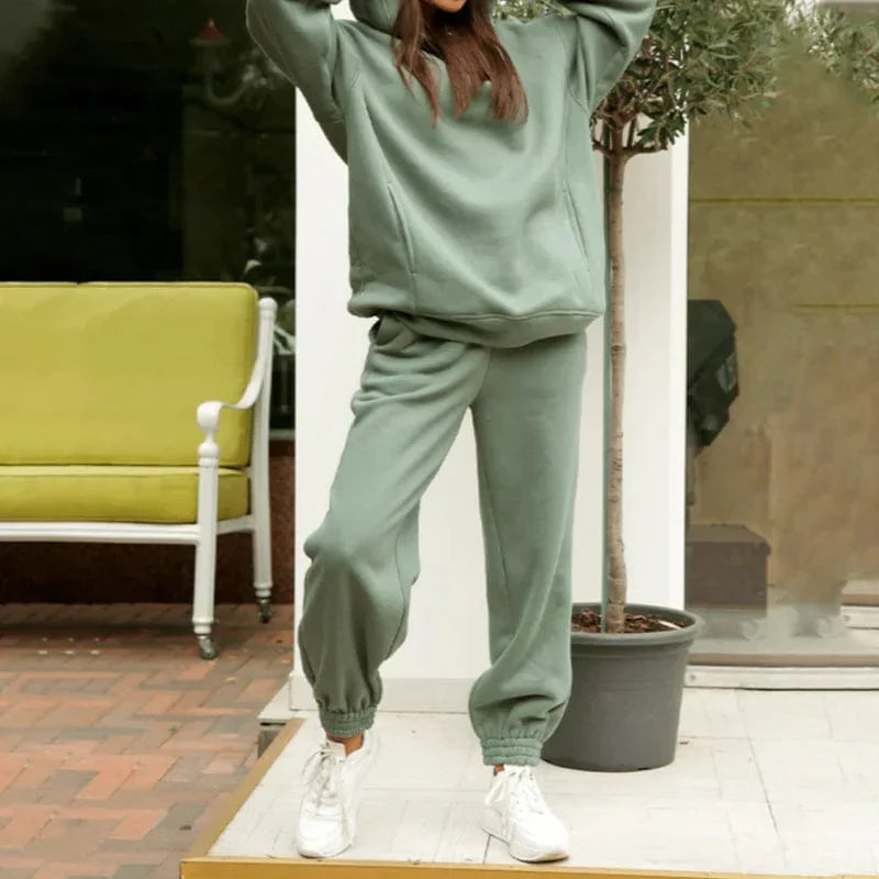 Woman in green oversized sweatshirt and jogger set, standing outdoors. Casual loungewear fashion, comfortable and stylish outfit, white sneakers.