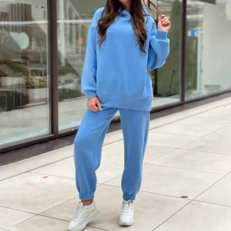 Woman wearing a casual blue sweatshirt set with joggers and white sneakers, standing outdoors. Comfortable loungewear fashion for women.