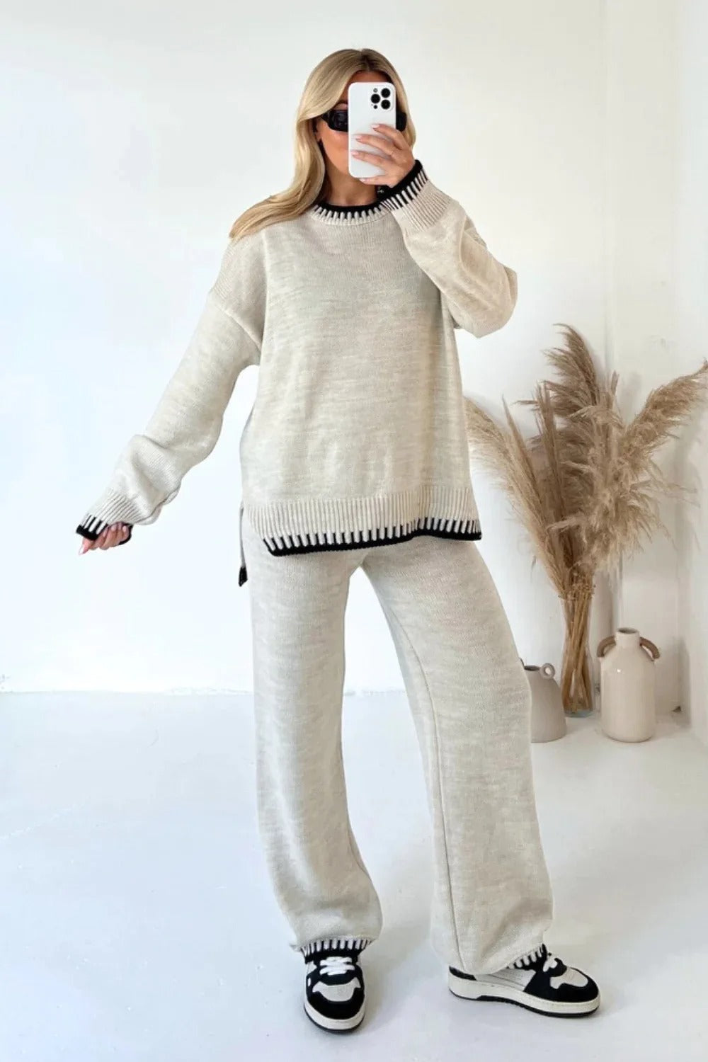 Woman in cozy beige knit loungewear set with black trim, taking a mirror selfie. Stylish casual outfit, perfect for fall fashion trends.