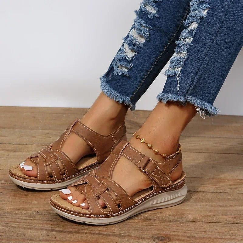 Brown leather sandals on woman's feet, paired with distressed blue jeans. Comfortable, stylish footwear for casual summer fashion.