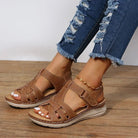 Brown leather sandals on woman's feet, paired with distressed denim jeans. Comfortable, stylish footwear for casual summer fashion.