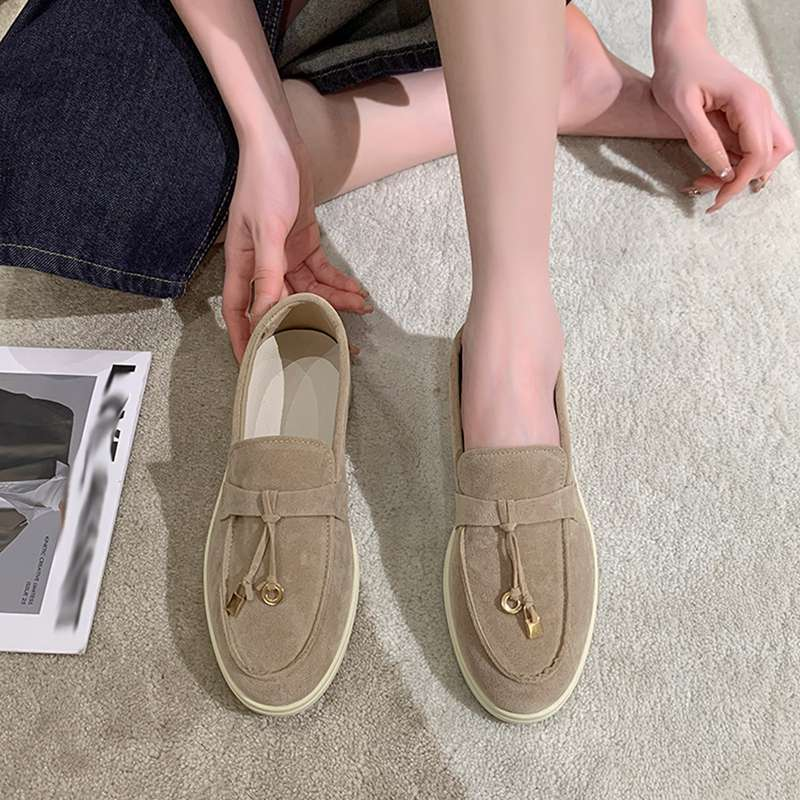 Beige suede loafers with tassel detail on a carpeted floor, worn by a person. Casual footwear, stylish design, comfortable shoes for everyday wear.