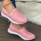 Pink slip-on sneakers with white soles, featuring breathable mesh fabric, worn on a wooden floor. Stylish casual footwear for women.