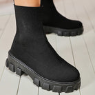 Black sock boots with chunky platform sole on white wooden floor; trendy women's footwear, stylish knit design, comfortable and modern fashion.