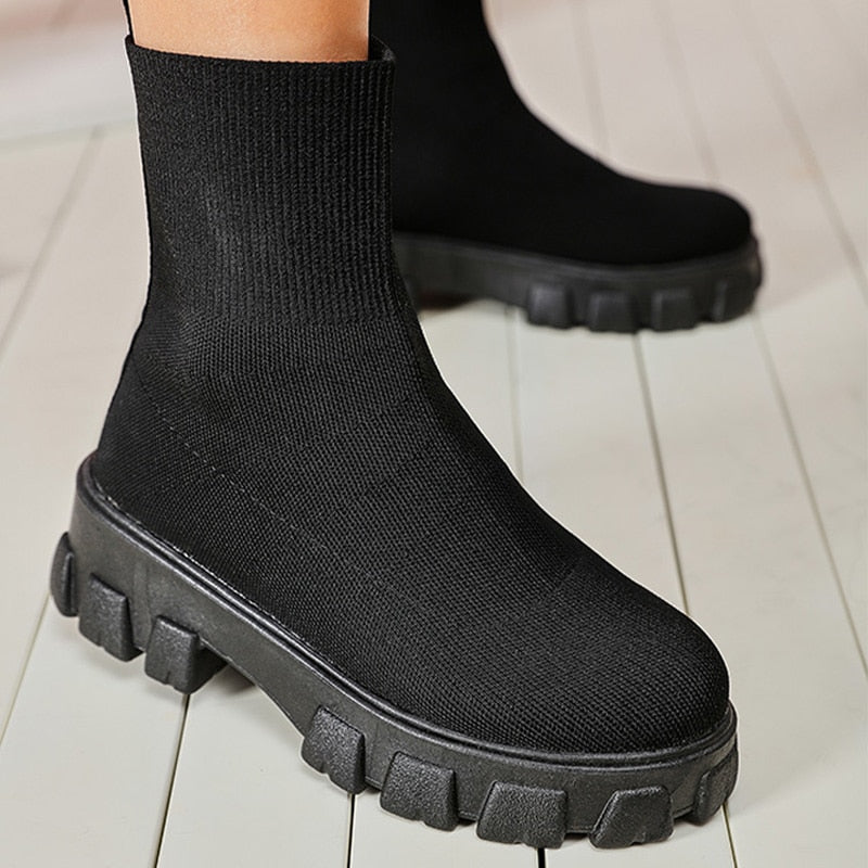 Black sock boots with chunky platform sole on wooden floor; stylish women's footwear, trendy fashion boots, comfortable knit design.