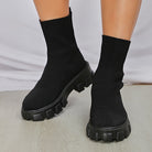 Black sock boots with chunky platform soles on a wooden floor, showcasing trendy women's footwear, perfect for fashion-forward style and comfort.