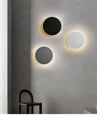 Modern circular wall lights with black, gray, and white panels on a minimalist gray wall, illuminating a contemporary interior space.