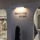 Modern boutique interior with 'Morning Studio' sign, minimalist design, clothing racks, and cactus decor, highlighting contemporary retail space.