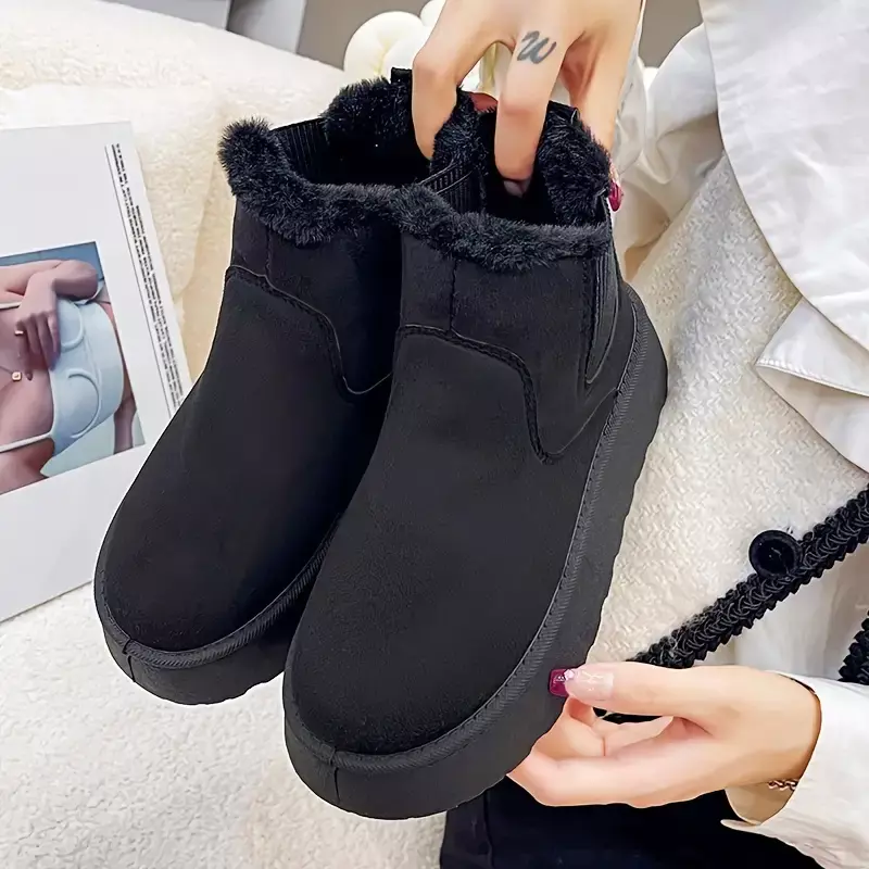 Black winter boots with faux fur lining, slip-on design, held by a person. Cozy footwear for cold weather. Ideal for casual, stylish comfort.