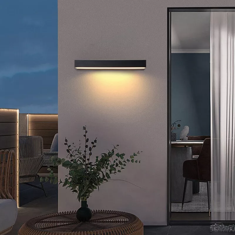 Modern outdoor wall light fixture illuminating a patio area at dusk, featuring sleek black design and warm LED lighting. Perfect for contemporary home exteriors.