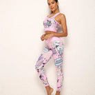 Woman in pink comic-style activewear set, featuring a sports bra and leggings with vibrant pop art graphics, standing against a white wall.