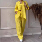 Woman wearing a stylish yellow linen two-piece outfit with a button-up shirt and wide-leg pants, standing indoors on a wooden floor.