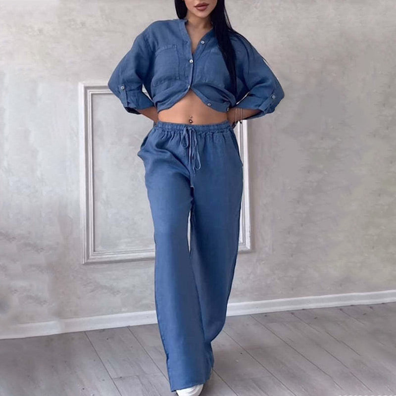 Woman wearing a stylish blue denim co-ord set with a cropped button-up shirt and high-waisted pants, standing on a light wooden floor.