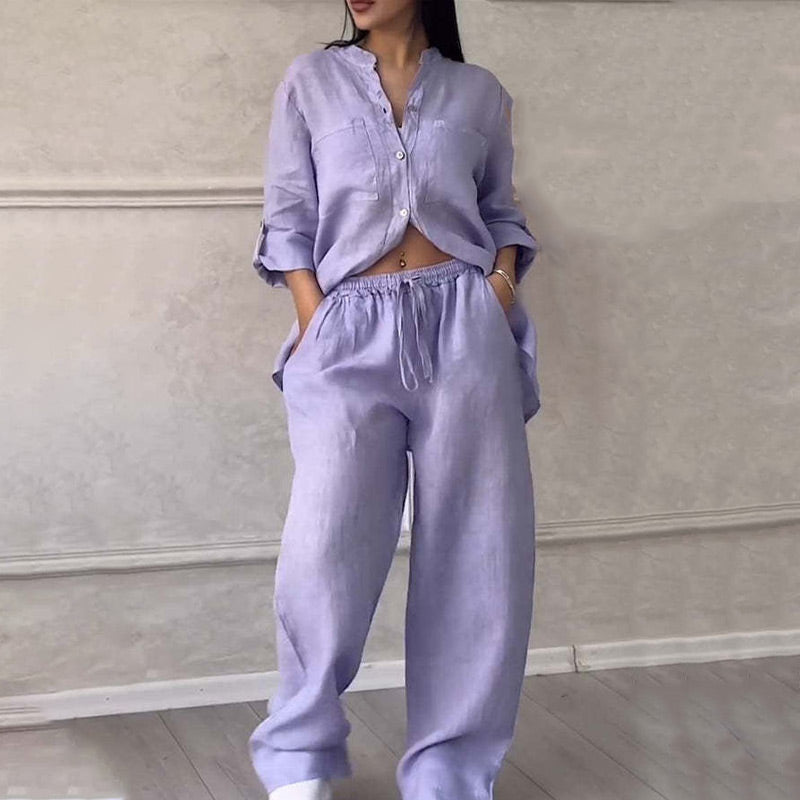 Woman wearing a stylish lavender linen two-piece outfit with a button-up top and drawstring pants, standing against a neutral background. Fashionable loungewear.