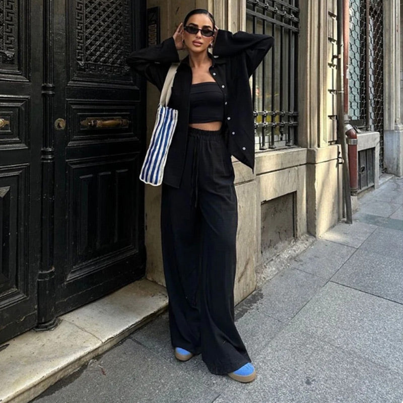 Fashionable woman in black outfit with striped tote bag, standing confidently on urban street. Trendy street style, chic fashion, modern urban look.