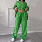 Woman wearing a stylish green two-piece loungewear set with button-up top and drawstring pants, standing indoors on wooden floor.