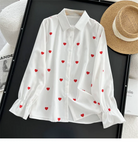 White button-up shirt with red heart pattern on black background, accompanied by a straw hat. Perfect for casual fashion and summer style.