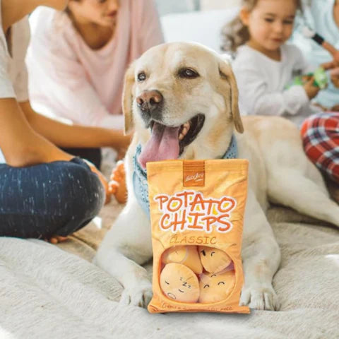 Golden retriever holding a bag of classic potato chips, surrounded by people, in a cozy home setting. Snack time, family, and pet-friendly atmosphere.