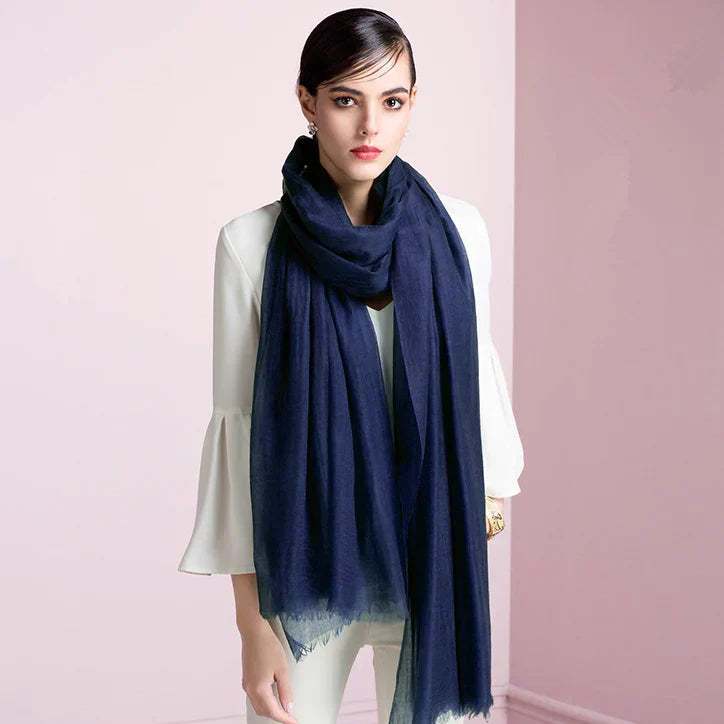 Woman wearing elegant navy blue scarf over white blouse, standing against a soft pink background. Fashionable accessory, stylish outfit.