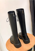 Black knee-high leather boots with side zippers and lace-up detail on a wooden stool. Stylish women's footwear, perfect for fall fashion trends.