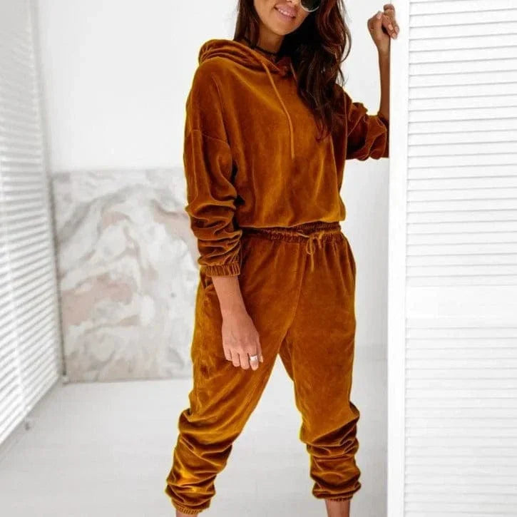 Woman wearing a brown velour sweatshirt set with hood and jogger pants, standing indoors. Fashionable loungewear, cozy outfit, casual style.