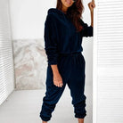 Woman wearing a navy blue velour sweatshirt set, featuring a hoodie and jogger pants, standing indoors. Fashionable loungewear outfit.