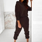 Woman wearing a black velour sweatshirt set, featuring a hooded top and jogger pants, standing indoors. Fashionable loungewear outfit.
