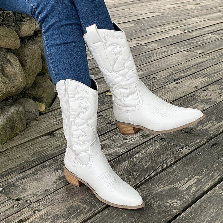 White women's cowboy boots with side zipper, high-quality leather, worn with blue jeans on a wooden deck. Fashionable footwear 2023.