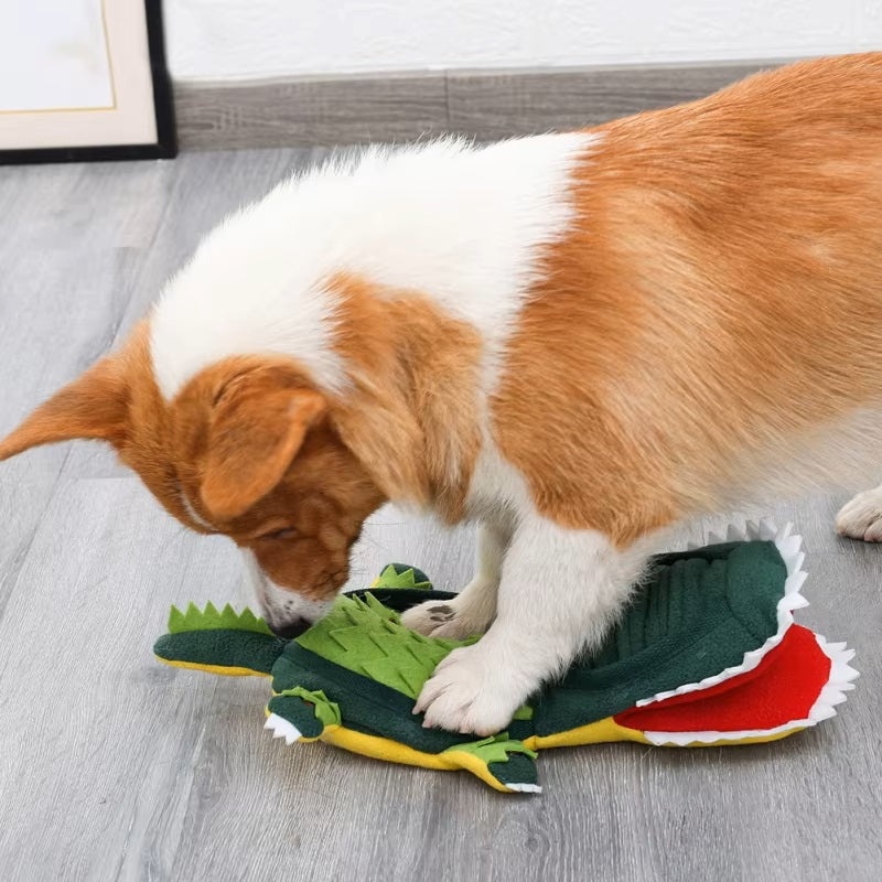 Corgi playing with a green dinosaur plush toy on a wooden floor, showcasing pet-friendly, durable dog toys for playful and active dogs.