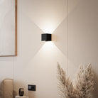 Modern black wall sconce light fixture on beige wall, minimalist interior design, geometric art, pampas grass decor, contemporary home lighting.