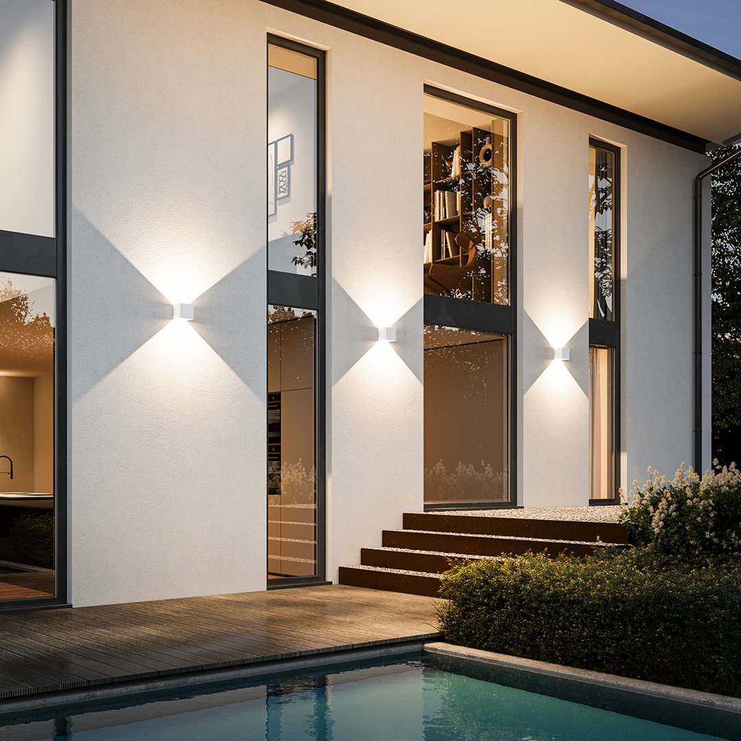 Modern minimalist house exterior with large glass windows, illuminated by sleek wall lights, overlooking a serene pool and landscaped garden.