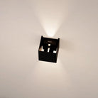 Modern black wall sconce with geometric design, illuminating a white wall. Contemporary lighting fixture, minimalist home decor, LED wall light.