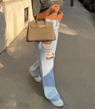 Woman wearing ripped loose jeans with large holes, holding a designer handbag, walking on a city sidewalk. Fashionable street style outfit.