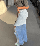 Woman wearing light blue ripped wide-leg jeans with large holes, paired with a black crop top, standing on a city sidewalk. Fashionable streetwear.