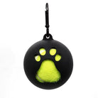 Black silicone dog ball holder with paw-shaped cutout, featuring a bright yellow tennis ball inside. Pet accessory, durable, portable design.