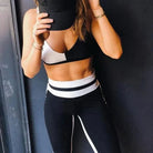 Woman in stylish black and white sportswear set, featuring a color-blocked sports bra and leggings, holding a cap. Fitness fashion, activewear.